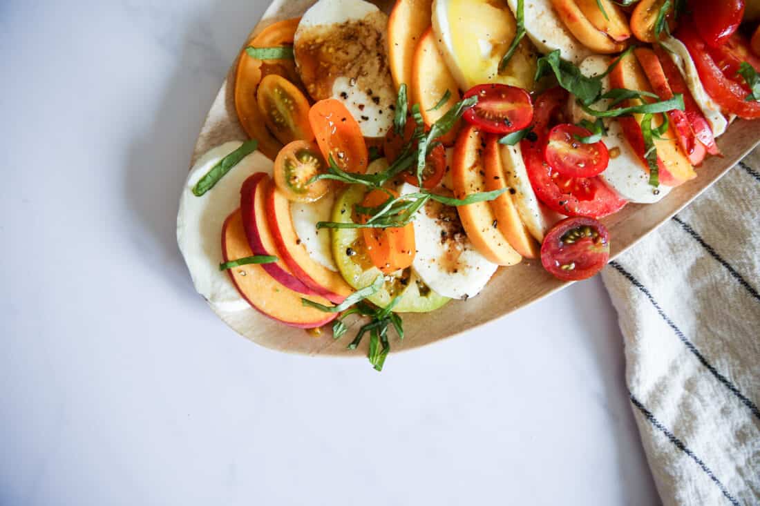 Peach caprese salad on a white plate with a white towel with blue stripes