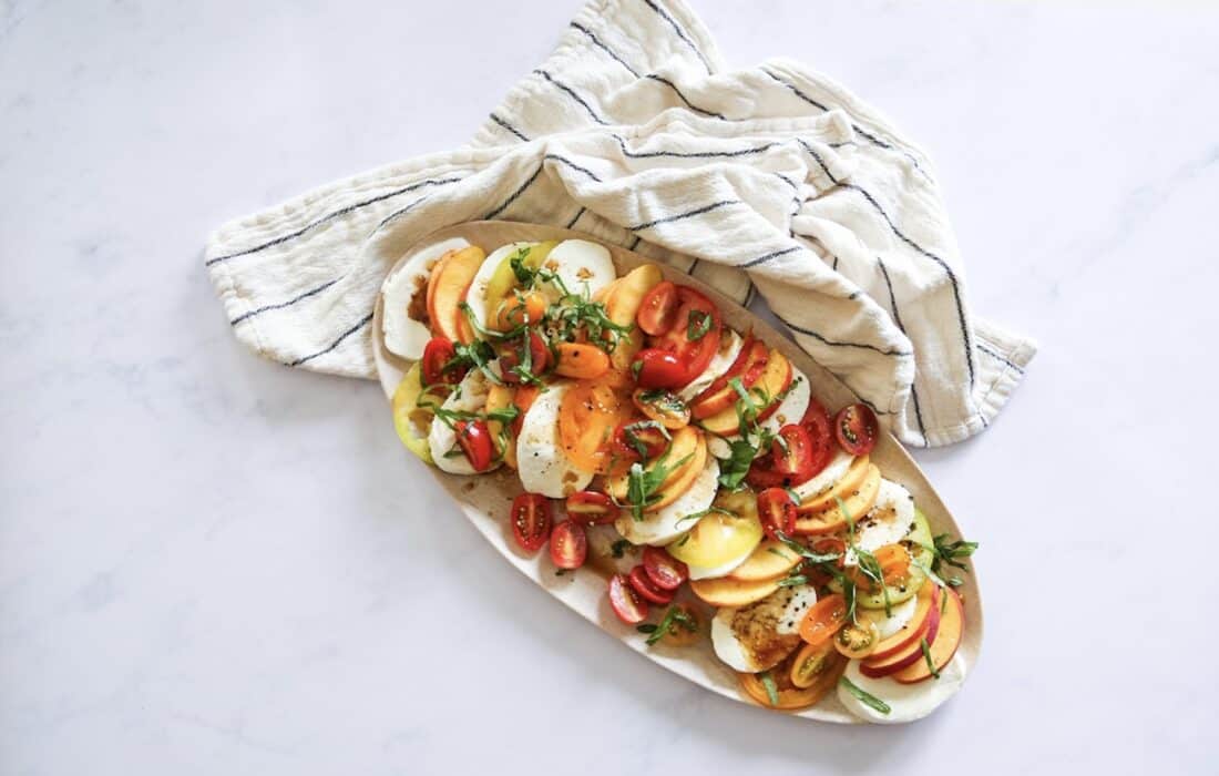 Plated peach caprese salad with drizzled olive oil and and white and blue-striped towel 