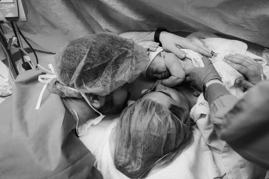 a woman and man holding a baby being delivered via c-section