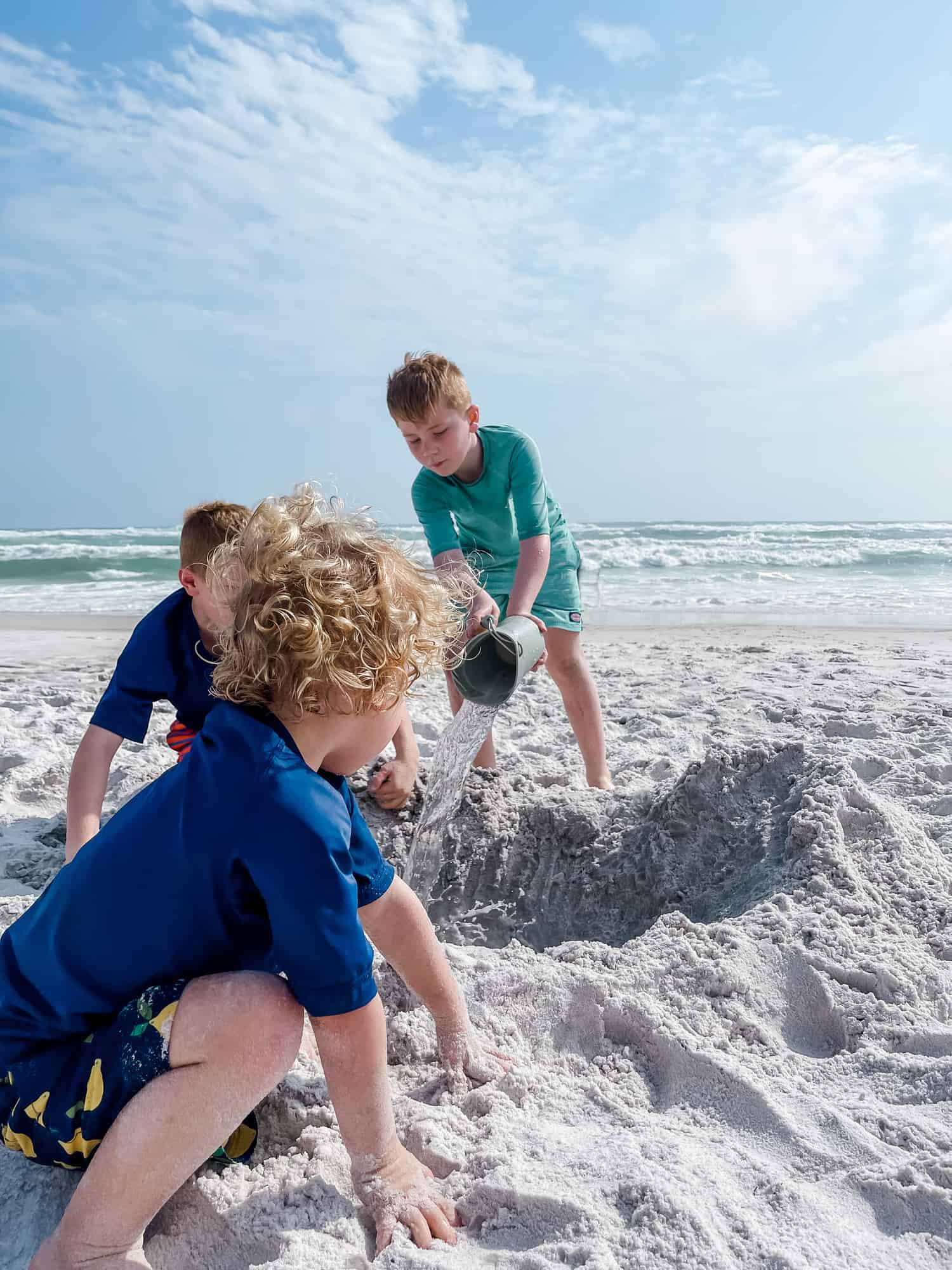 three boys digging a hole in the sand on the beach 