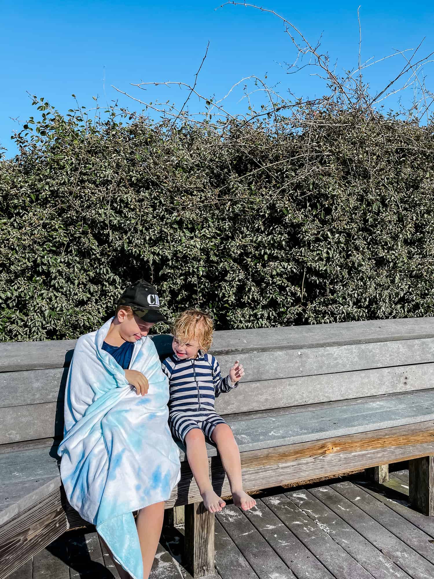 two boys on a bench, on wrapped in a beach towel 