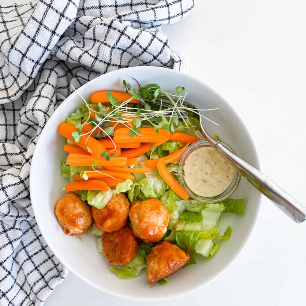 baked chicken meatballs in a white bowl on top of greens for a salad