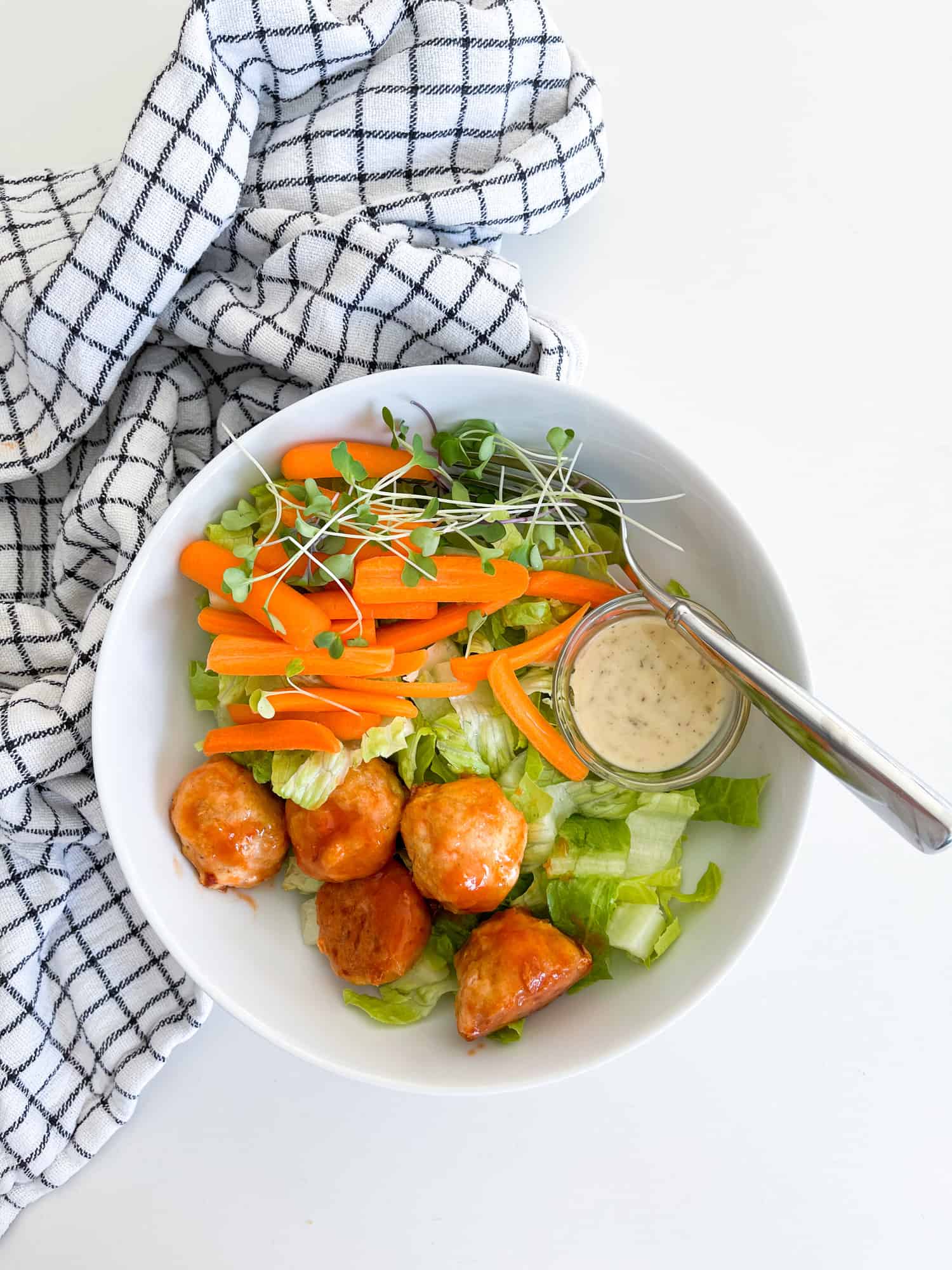 baked chicken meatballs in a white bowl on top of greens for a salad