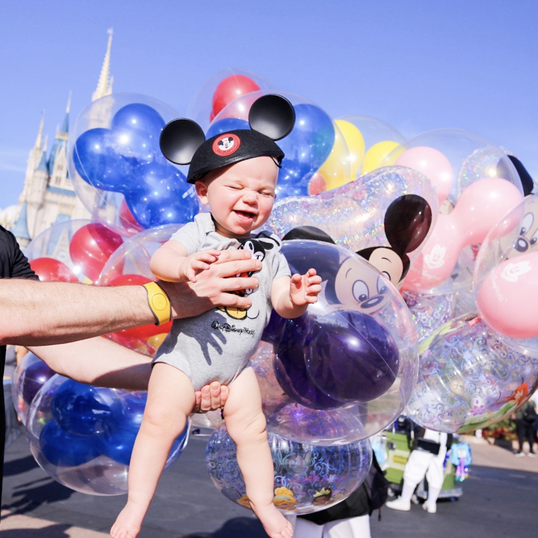 a baby boy being held in front of balloons smiling at Disney