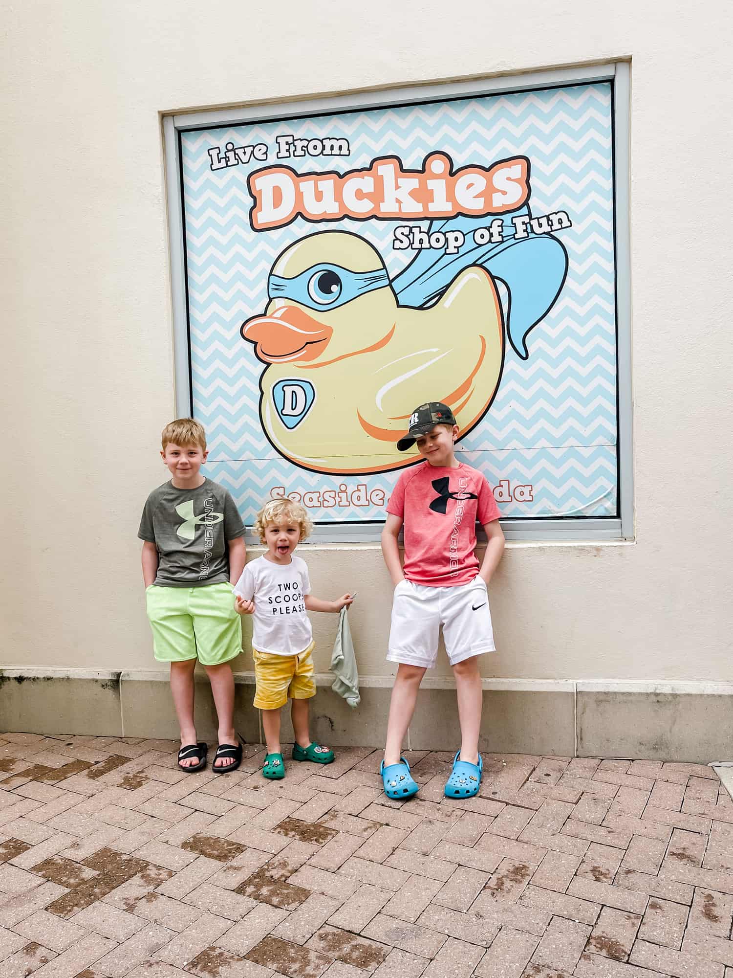 three boys standing against a wall next to a sign the reads "live from duckies shop of fun"
