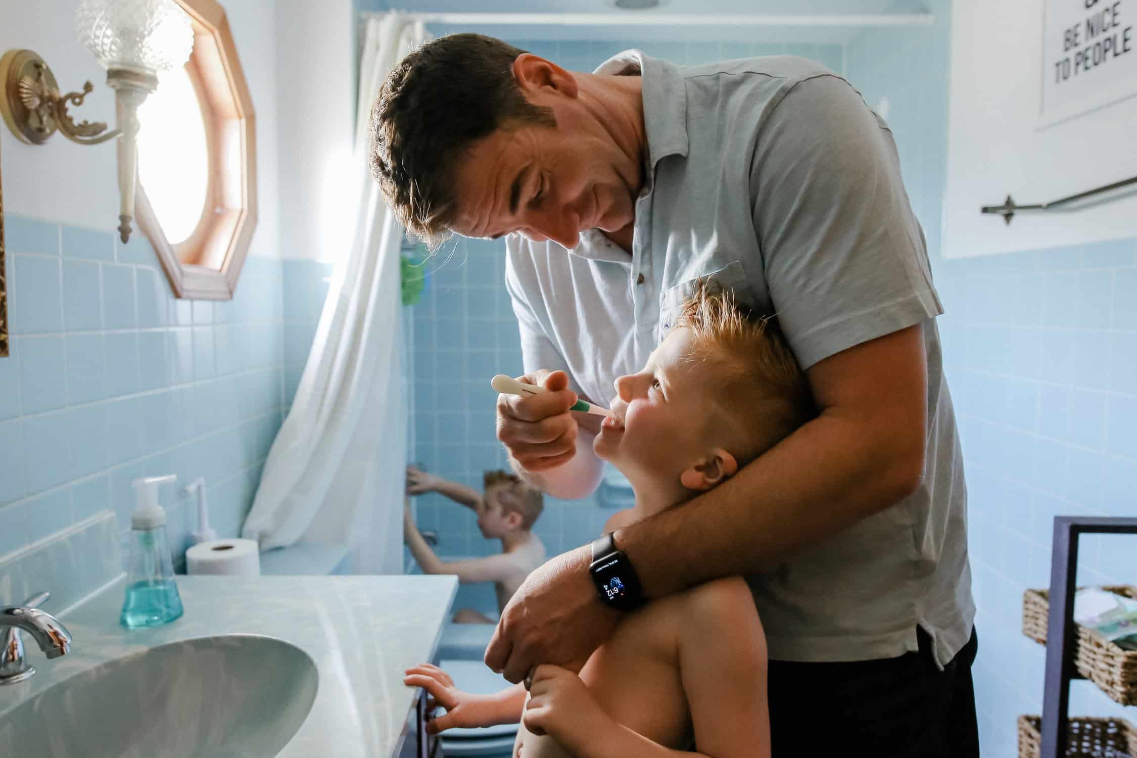a dad helping his young son brush his teeth