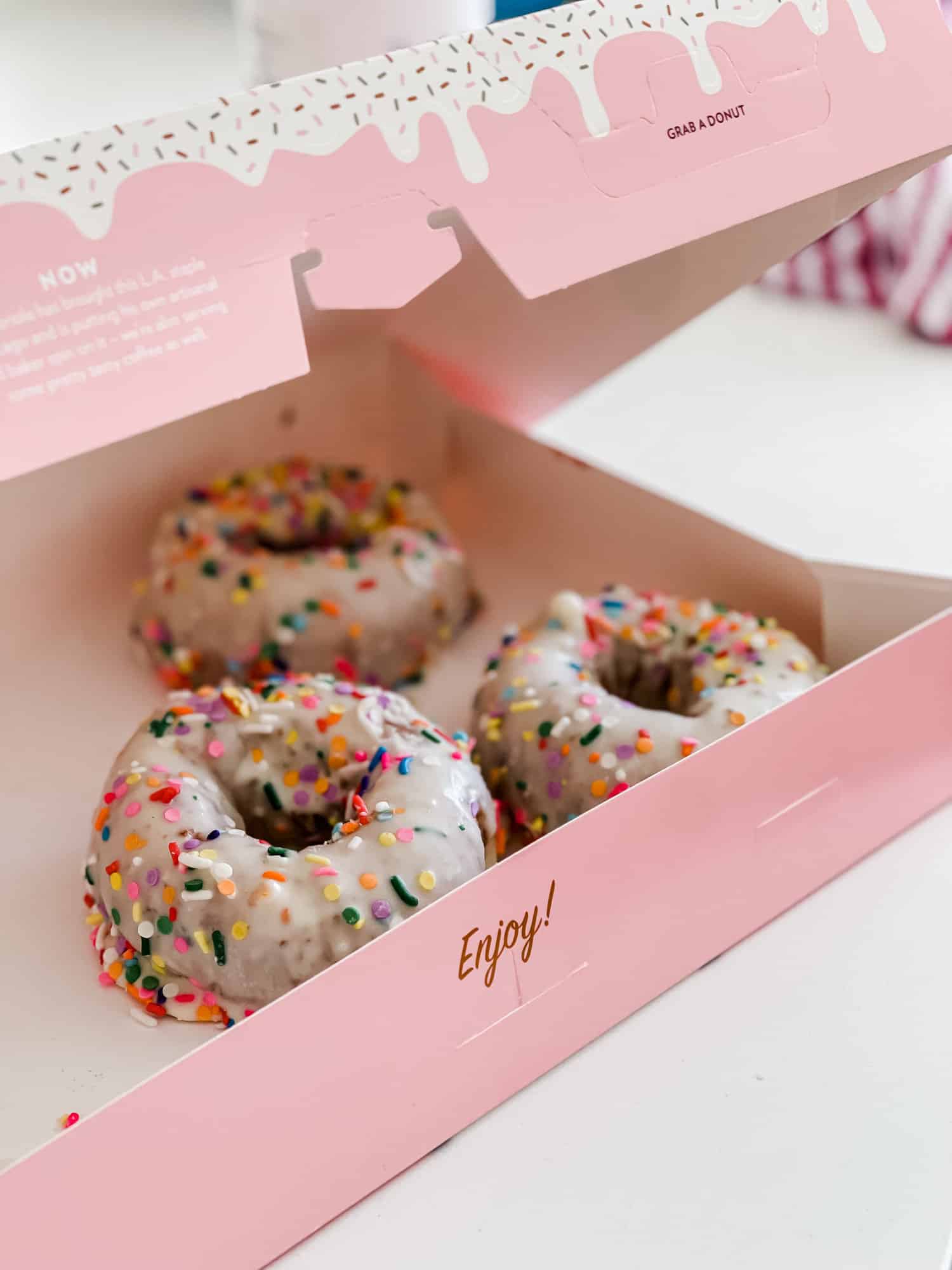 a pink box of white frosted donuts topped with sprinkles