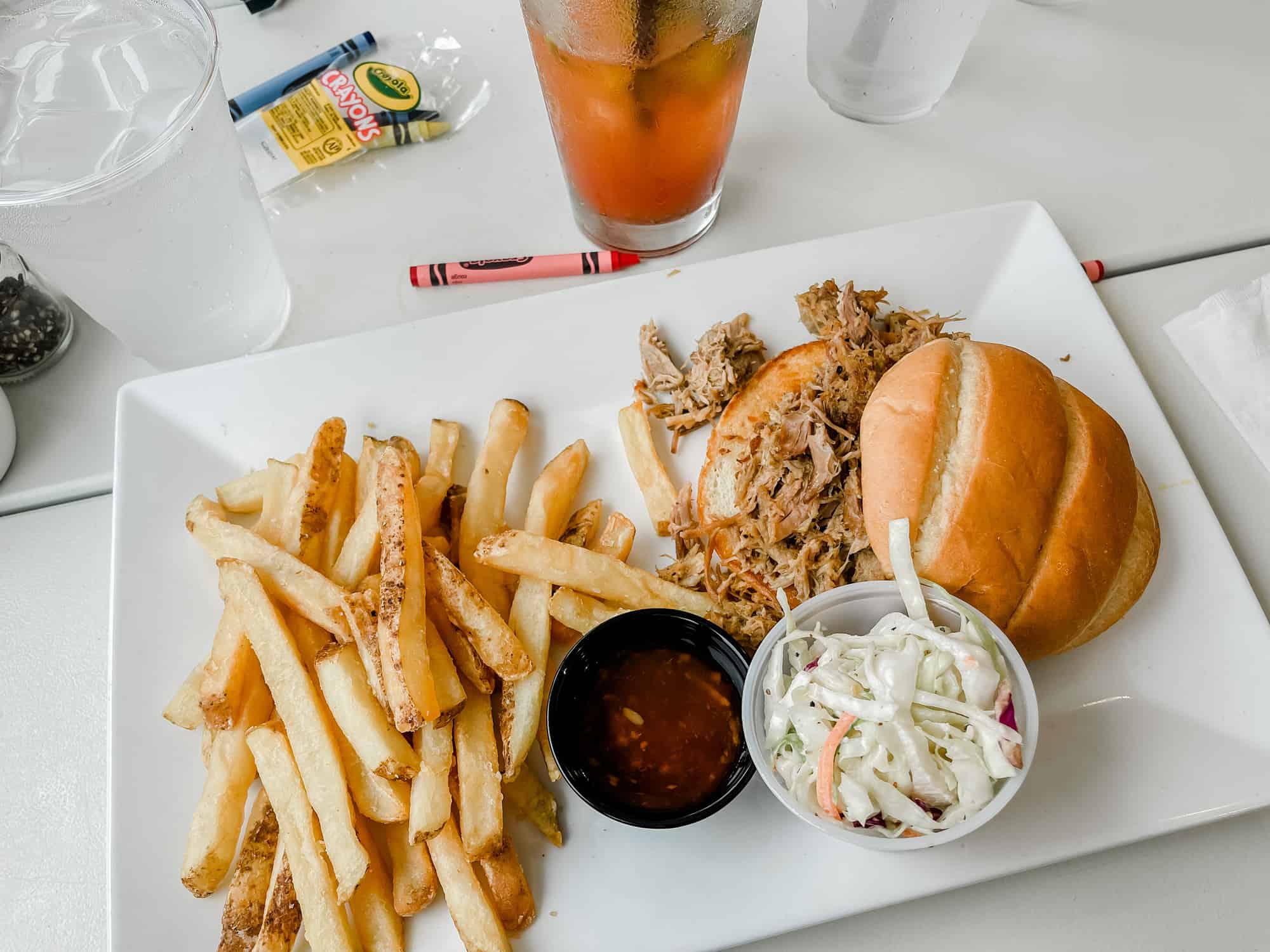 fries, coleslaw, and a pulled pork sandwich on a white plate