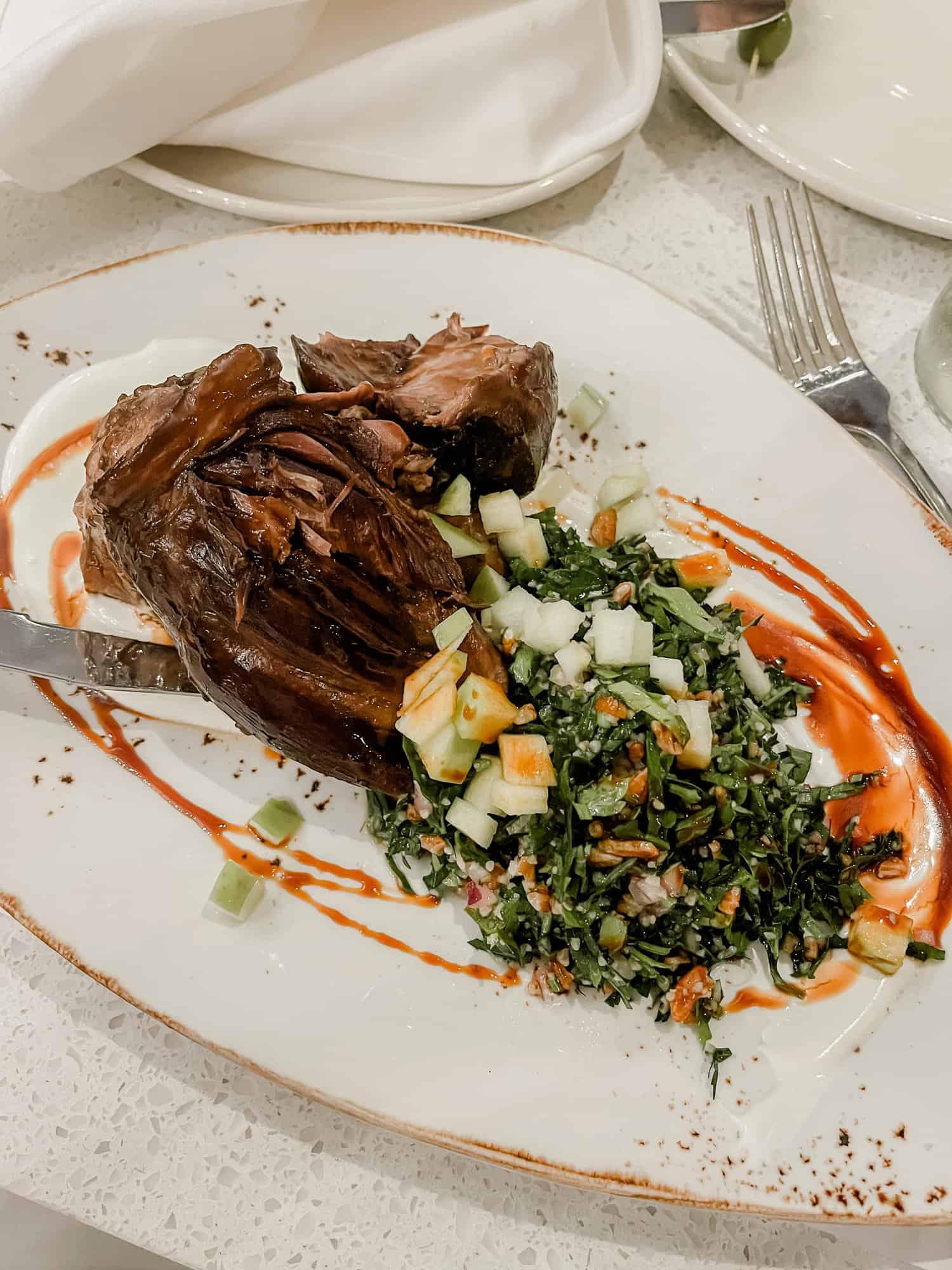 steak with tabbouleh salad on a white plate with an orange and red sauce around the edges