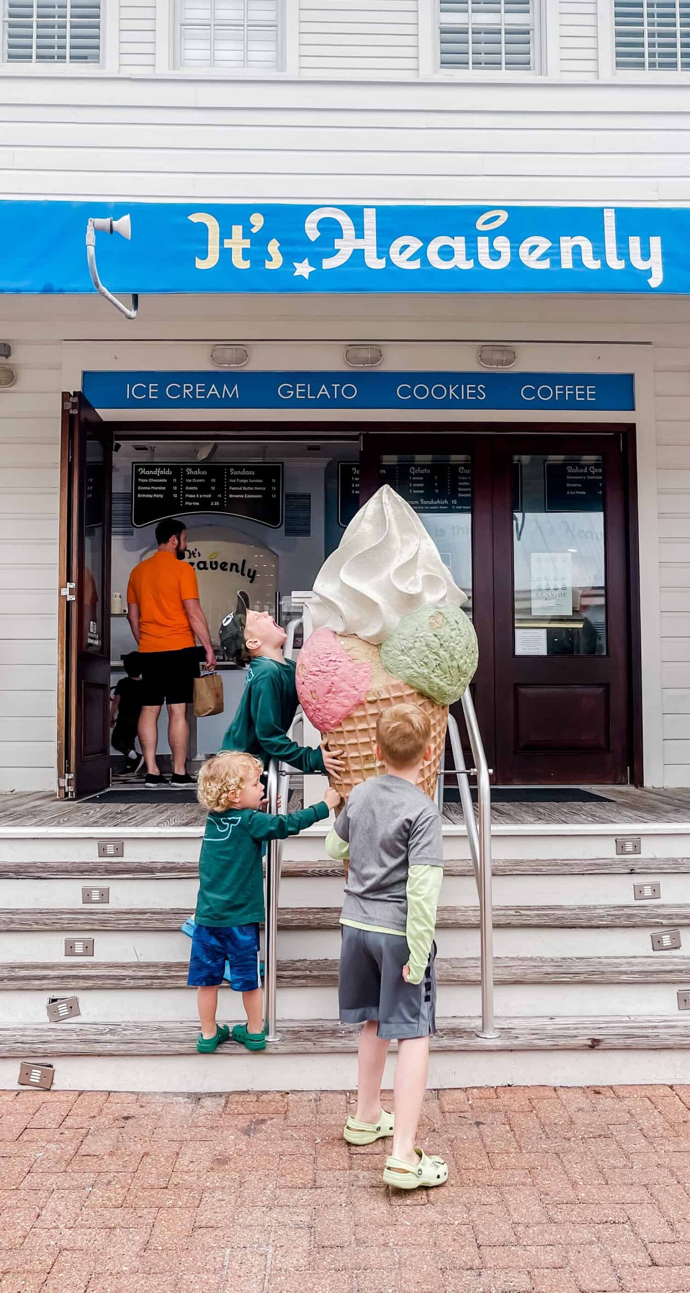 three boys on stairs leading up to an ice cream shop pretending to lick an ice cream statue 