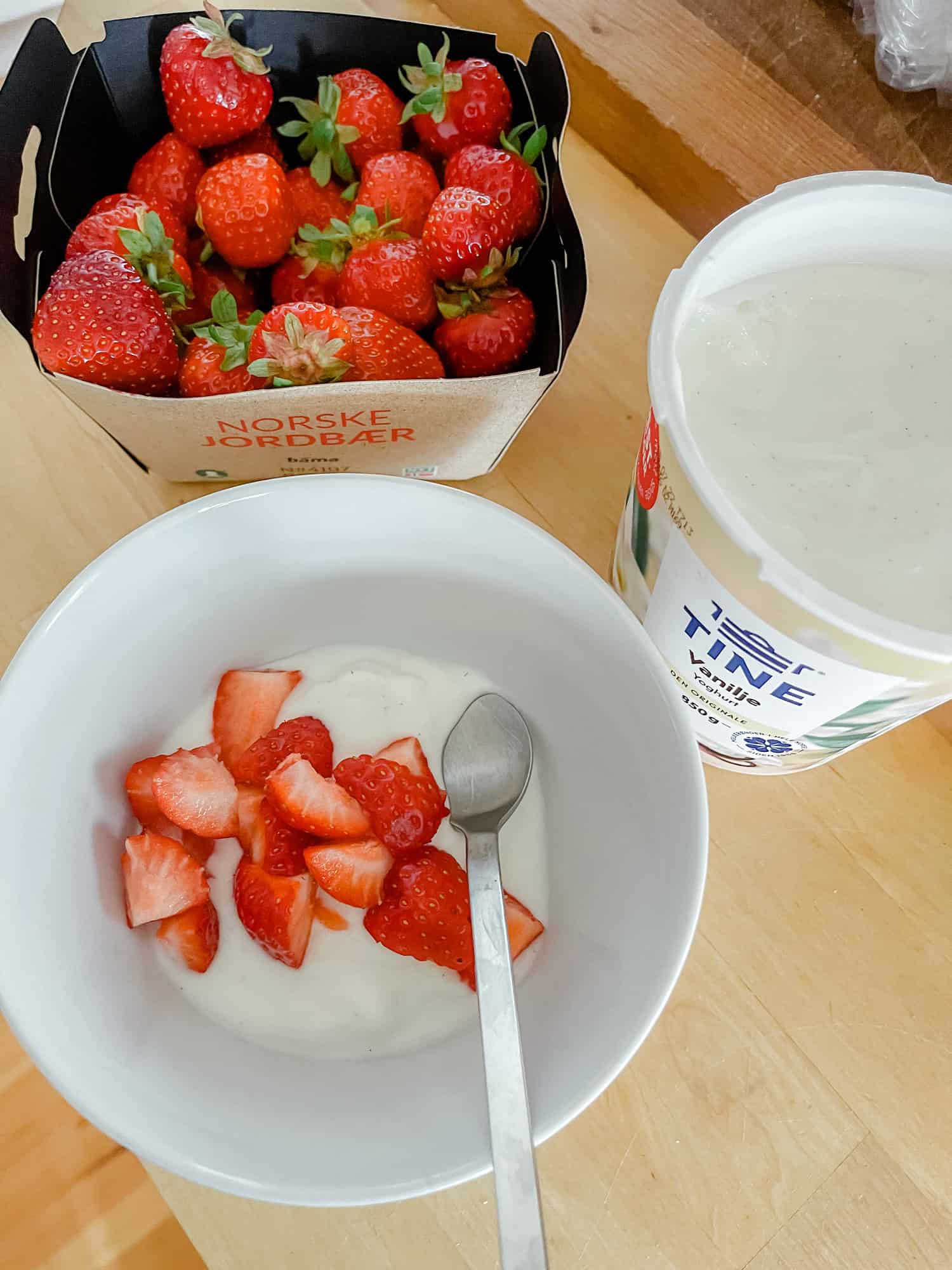 a white bowl full of yogurt and sliced strawberries with a tub of yogurt and whole strawberries on the side