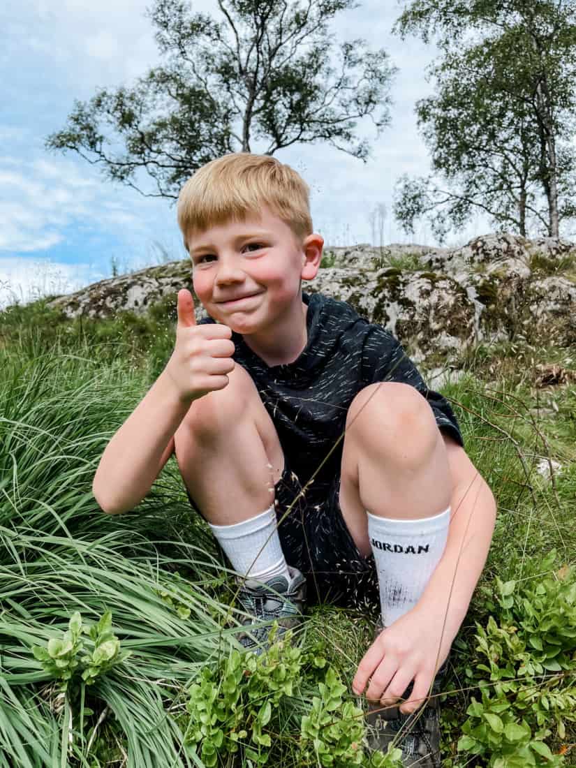 a boy squatting in the grass making a thumbs-up sign