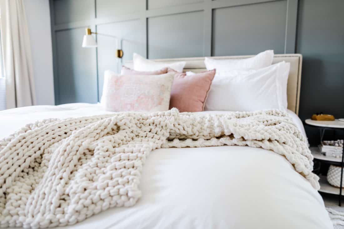 close up image of a bed with a white duvet, cream knit blanket and light pink throw pillows