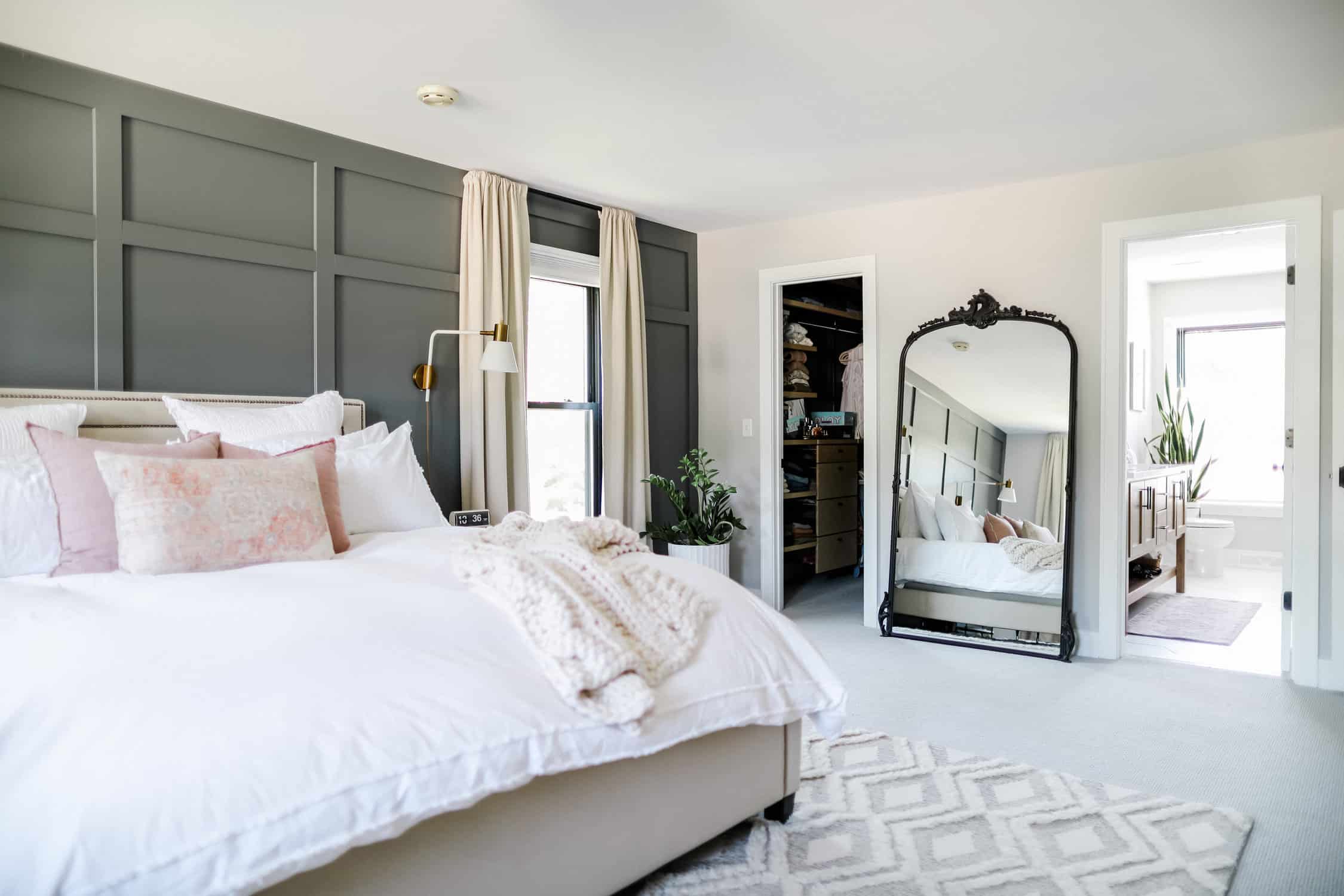 bedroom with a large bed with a white duvet, white black out curtains, and a mirror