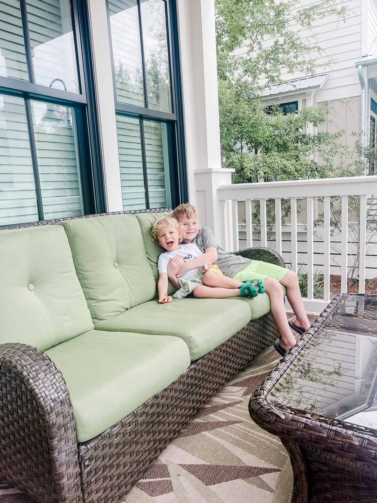 two boys sitting on a couch on a porch hugging