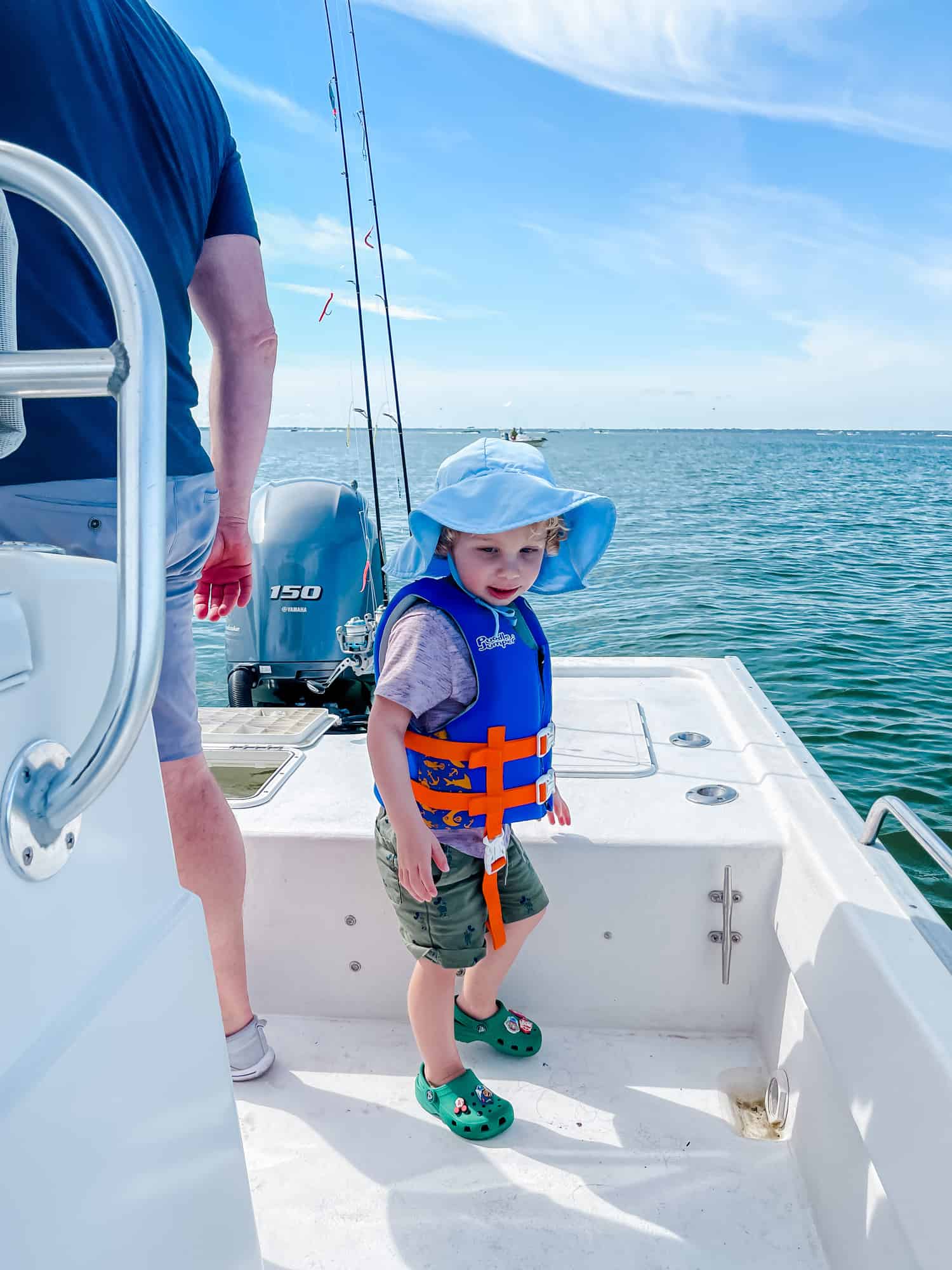 a little boy on a boat in a life jacket with a sun hat on 