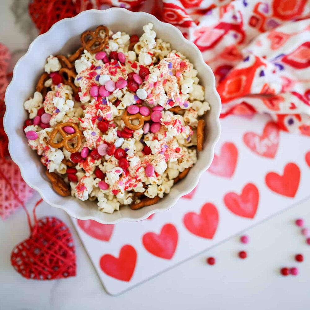 valentine's day popcorn mix in a white bowl with hearts around